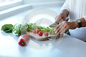 Hands on chopping board, vegetables and knife on table in kitchen cooking organic food. Woman cutting plants on counter