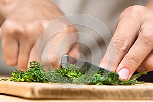 Hands chopping fresh dill on the cutting board
