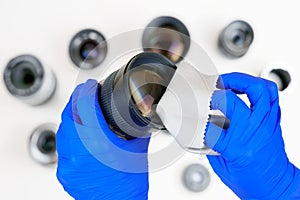 Hands cleaning digital camera lens from dust with white cleaning cloth, set of lenses on a white surface