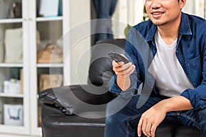Hands closeup Asian young man holding remote control and watching TV while sitting on the couch at home
