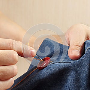 Hands of clothier sew button to a denim fabric close up