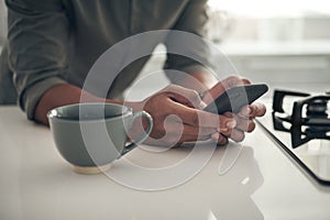 Hands, coffee and man with smartphone in kitchen for trending updates or popular topics on social media or internet