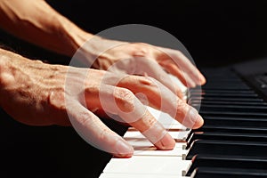 Hands of composer play the keys of the piano on black background close up