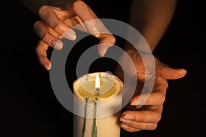 Hands conjure over a candle on a black background, close-up. Spiritual session, clairvoyant fortune teller at work