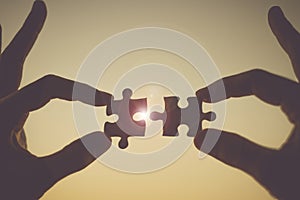 Hands connecting couple puzzle piece against sunrise effec