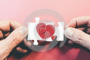 Hands connecting or disconnecting jigsaw puzzle pieces with red heart photo