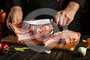 The hands of a cook or a butcher with a knife in the kitchen cut the ribs. Cooking a delicious grill for a restaurant or hotel