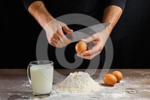 Hands of the cook close-up, breaks the egg into flour, a glass of fresh milk, cooking dough on a dark background