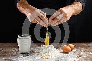 Hands of the cook close-up, breaks the egg into flour, a glass of fresh milk, cooking dough on a dark background