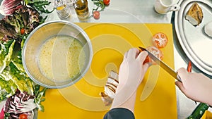 Hands of the cook cut a fresh tomato on a cutting board