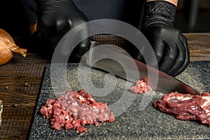 Hands of the cook in gloves cut the red meat on the board. nearby are tomatoes, onion, butter