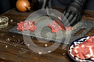 Hands of the cook in gloves cut the red meat on the board. nearby are tomatoes, onion, butter