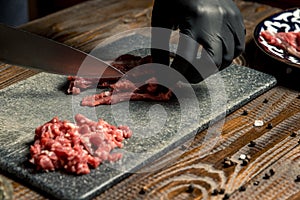 Hands of the cook in gloves cut the red meat on the board. nearby are tomatoes, onion, butter