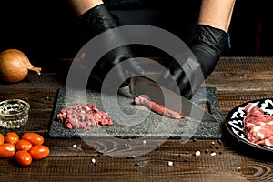 Hands of the cook in gloves cut the red meat on the board. nearby are tomatoes, onion, butter