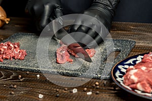 Hands of the cook in gloves cut the red meat on the board. nearby are tomatoes, onion, butter