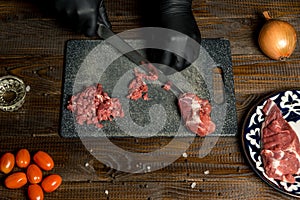 Hands of the cook in gloves cut the red meat on the board. nearby are tomatoes, onion, butter