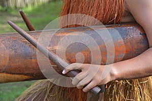 Hands of Cook Islander man plays music on a large wooden log Pat