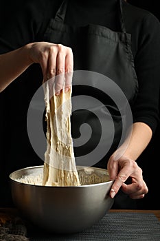The hands of the cook knead the dough on a black background, vertically