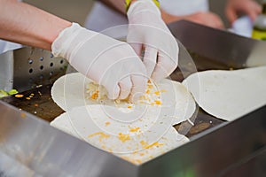 Hands of cook in latex gloves Sprinkling with cheese tortillas for preparing fresh fajita. Concept of national food