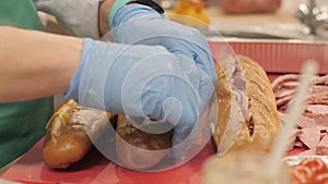 Hands cook putting pieces sausage in cut up baguette in fast food cafe