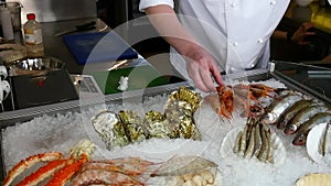 Hands of cook superimpose fresh shrimp and oysters on ice in seafood restaurant.