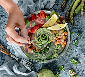 Hands cooking healthy superbowl or Buddha bowl with salad, baked sweet potatoes, chickpeas, broccoli, hummus, avocado, sprouts on