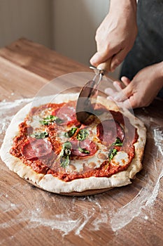 Hands cooks cut pizza with a special pizza knife on a wooden table with flour