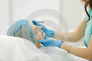 Hands of cosmetologist making preparation for face contouring plasty. Young woman gets beauty facial injections in salon