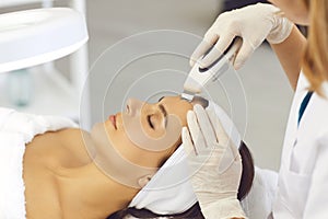 Hands of cosmetologist making professional ultrasound apparatus facial cleaning for woman