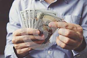 hands counting dollar banknotes on dark wooden surface