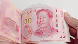 Hands counting a stack of hundred-dollar RMB banknotes