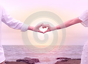 Hands of couple making heart sign on beach background