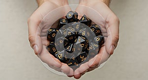 Hands cradle a collection of black polyhedral dice with gold numbers. These dice, photo