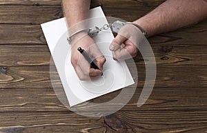 The hands of the criminal in handcuffs write with a pen on paper.