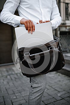 Hands of cropped unrecognisable man putting laptop in bag.