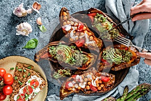 Hands cutting baked sweet potato toasts with roasted chickpeas, tomatoes, avocado, seedlings on wooden board. Healthy vegan food,