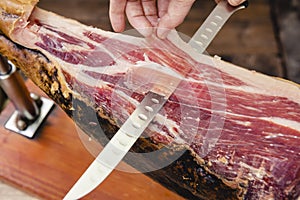 Hands cutting Iberian ham with knife