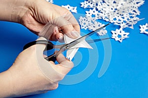 Hands cutting paper snowflakes over blue background