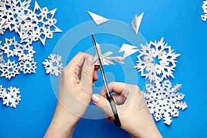 Hands cutting white paper snowflakes over blue