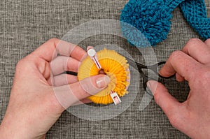 Hands Cutting Yellow Yarn Wrapped Around Pom-pom Maker