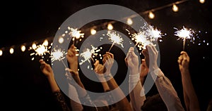 Hands in the dark waving sparklers. On backdrop of garland. New year, holiday, Christmas, birthday, party. Cheerful