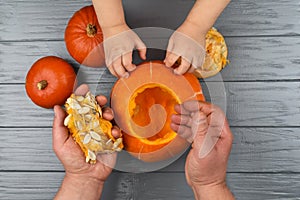 Hands of a daughter and father who pulls seeds and fibrous material from a pumpkin before carving for Halloween. Party