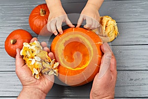 Hands of a daughter and father who pulls seeds and fibrous material from a pumpkin before carving for Halloween. Party