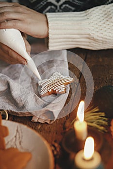 Hands decorating christmas gingerbread cookie star with frosting on rustic table with candle, spices, decorations. Atmospheric