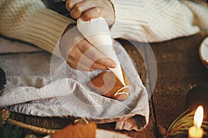 Hands decorating christmas gingerbread cookie tree with frosting on rustic table with napkin, candle, decorations. Atmospheric