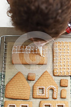 Hands decorating christmas gingerbread cookies with icing on table with candle and ornaments. Close up. Making