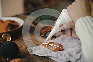 Hands decorating gingerbread cookie christmas tree with icing on rustic table with napkin, candle, decorations. Atmospheric moody