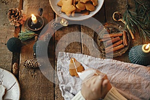 Hands decorating gingerbread cookie christmas tree with icing on rustic table with napkin, spices, candle, decorations. Top view.