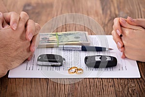 Hands on divorce document with wedding rings and car keys