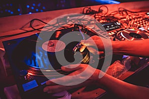 Hands of a DJ putting a vinyl record on a record player in a music club in the rays of blue and red light